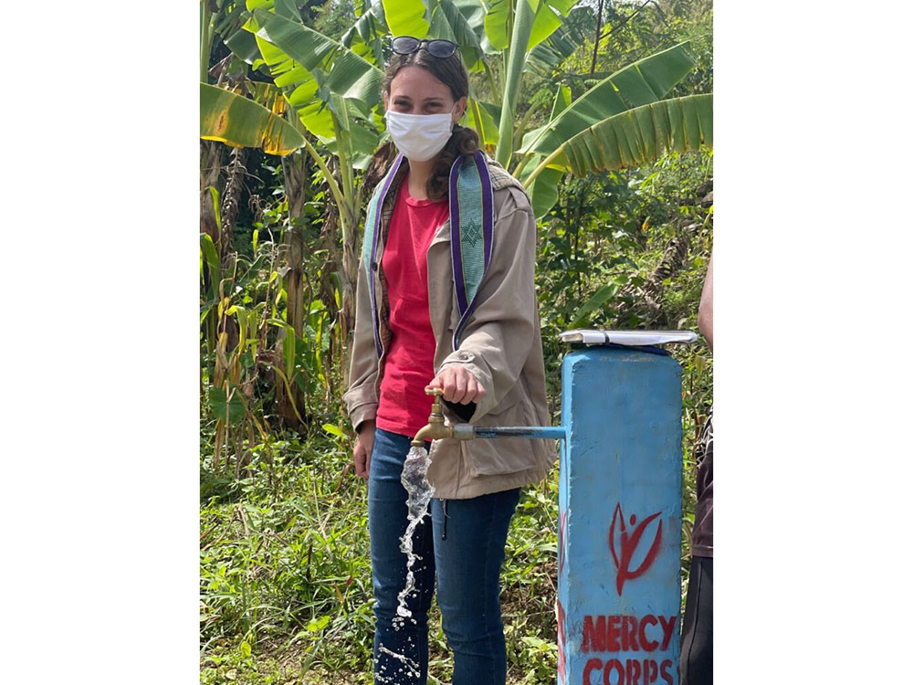 Kirsten Mandala next to an outdoor water spigot that's running with her hand on the handle.