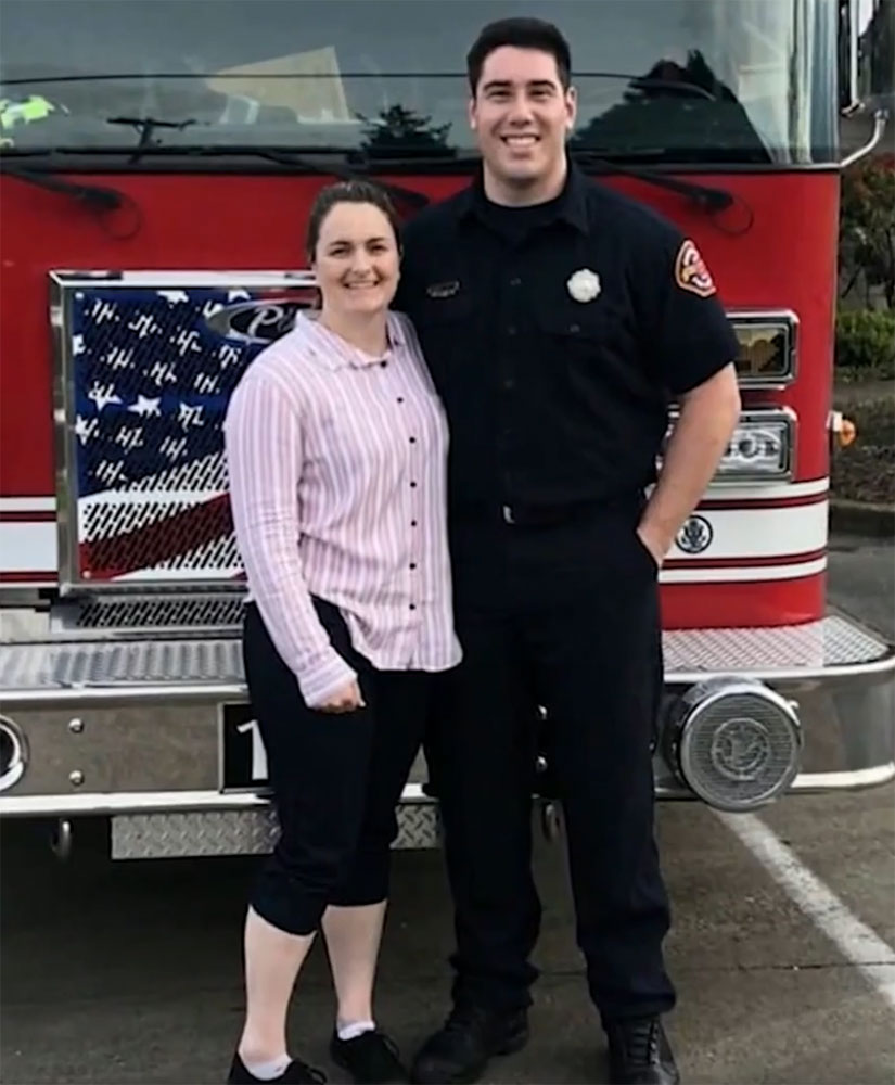 firefighter Michael Kienzle in uniform and standing next to a woman and a fireengine.