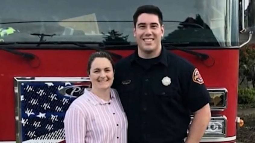 firefighter Michael Kienzle in uniform and standing next to a woman and a fireengine.