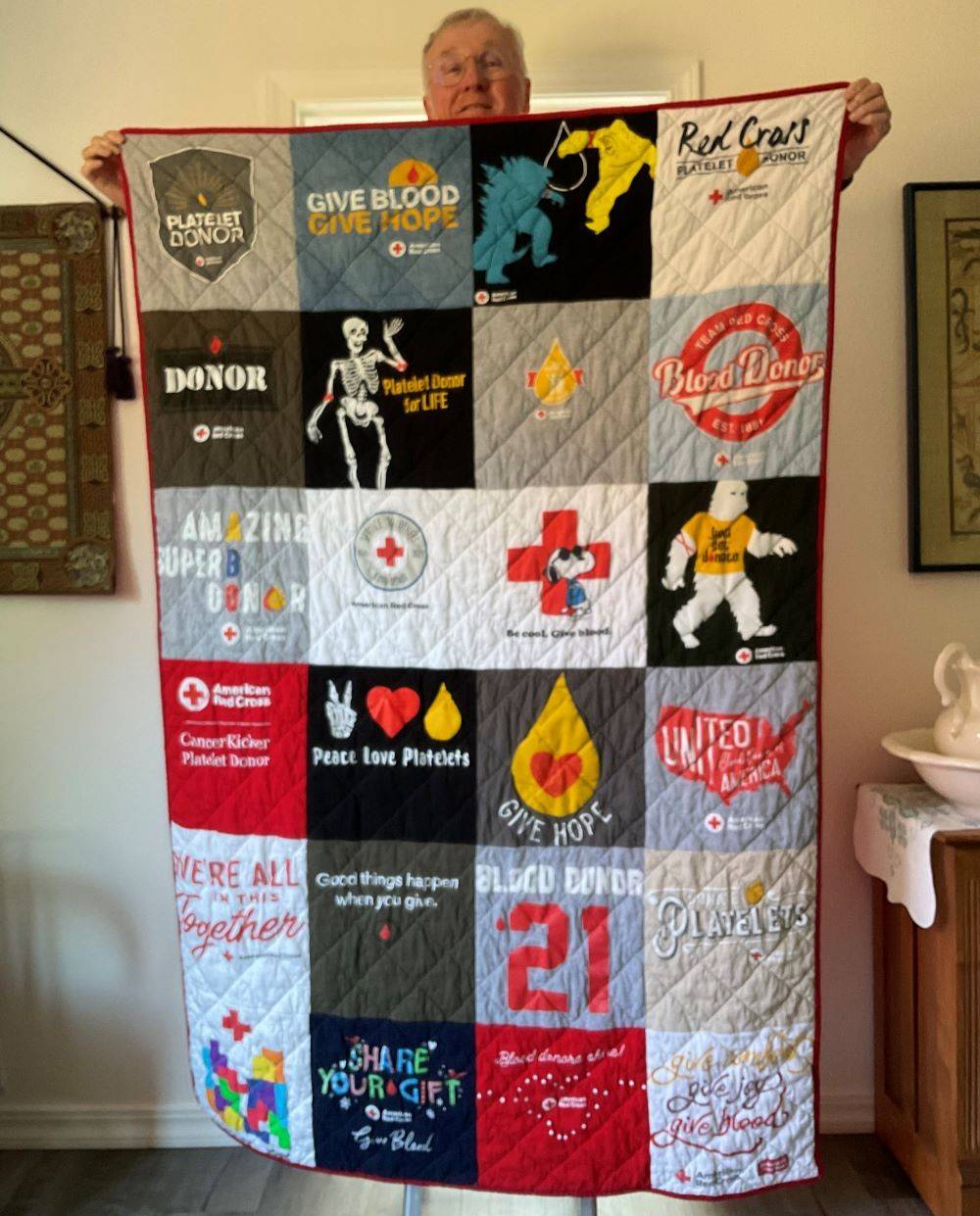 Mike holds up a quilt made up of Red Cross promotional T-shirts.