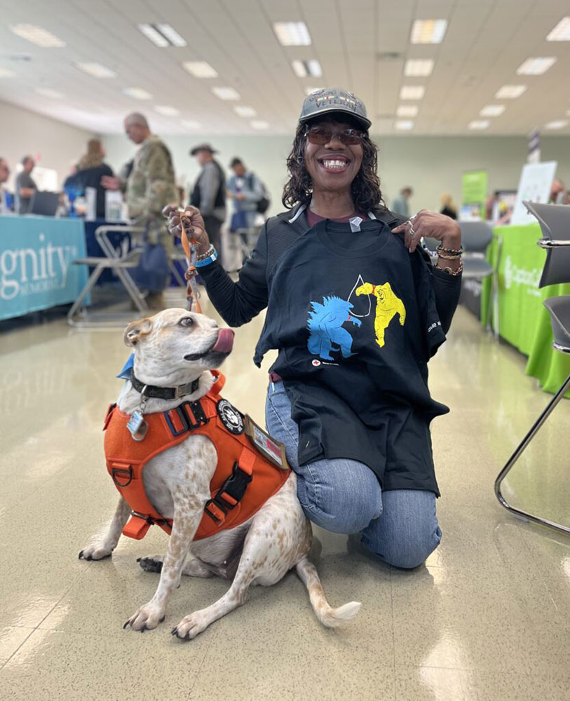 Killian Hough, holding a t-shirt up and holding the leash of her service dog "Hope."