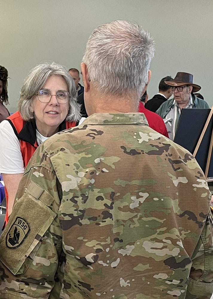 Red Cross volunteer Polly Waibel, speaking with a man in military jacket.