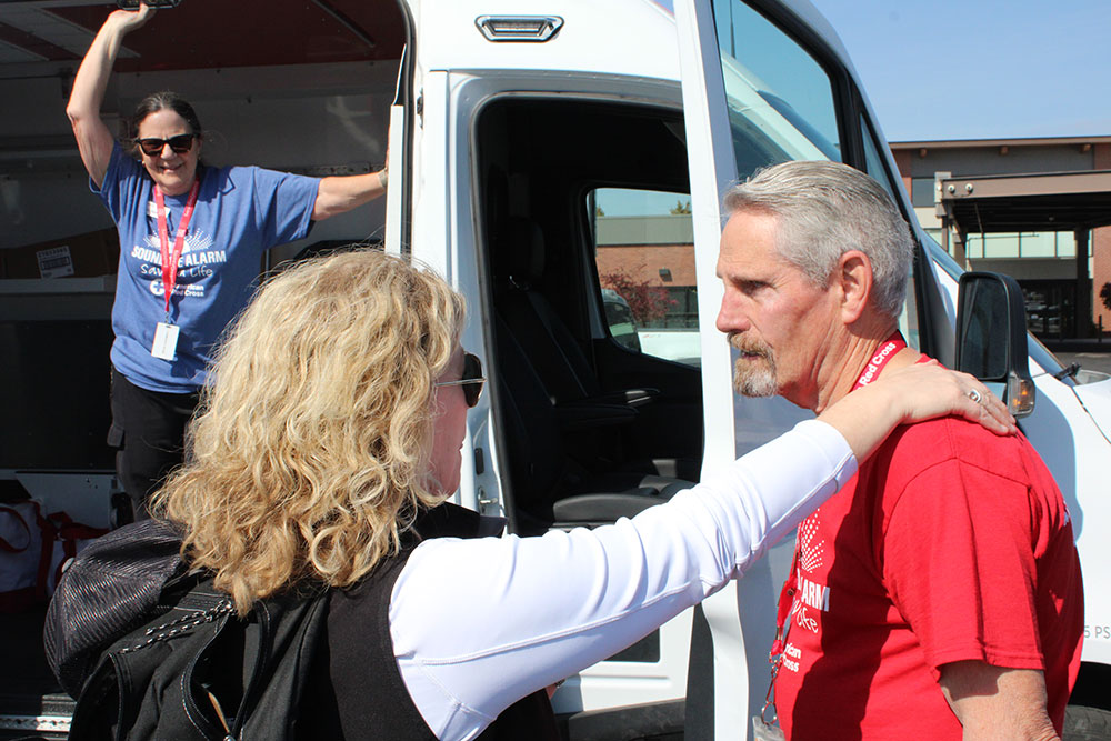 Three Red Cross volunteers talk to each other next to a Red Cross vehicle.