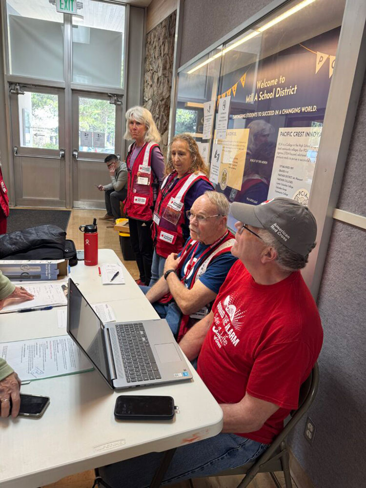 Red Cross volunteers sitting at a table with laptops and paperwork inside a room.