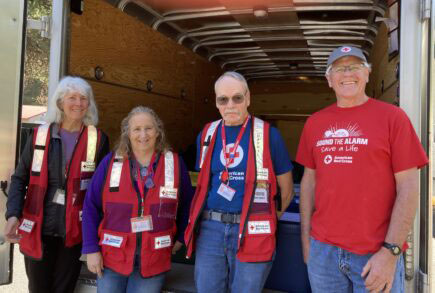 group photo of four Red Cross volunteers standing at the back of an open Red Cross trailer.