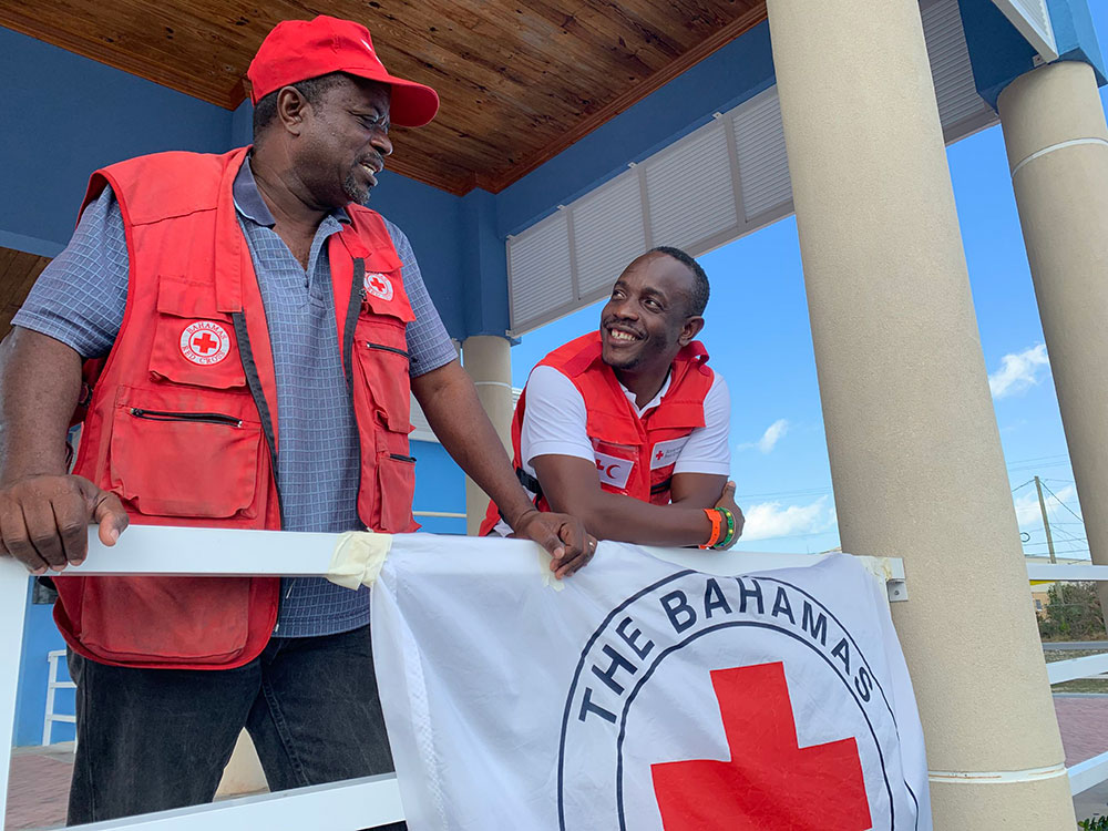 Two men in red vests stand beside a red cross flag.