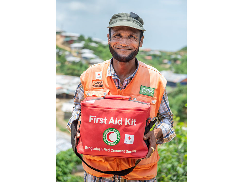 A man wearing an orange vest is holding a first aid kit.