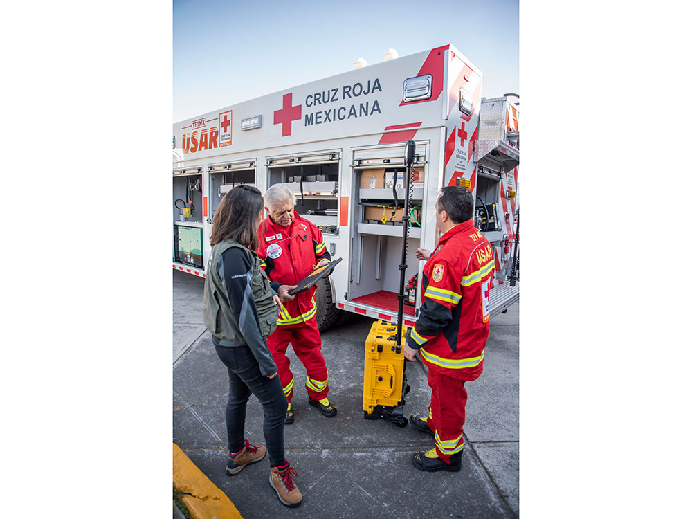 A Red Cross emergency medical services team in uniform, preparing equipment for a medical response in a community setting.