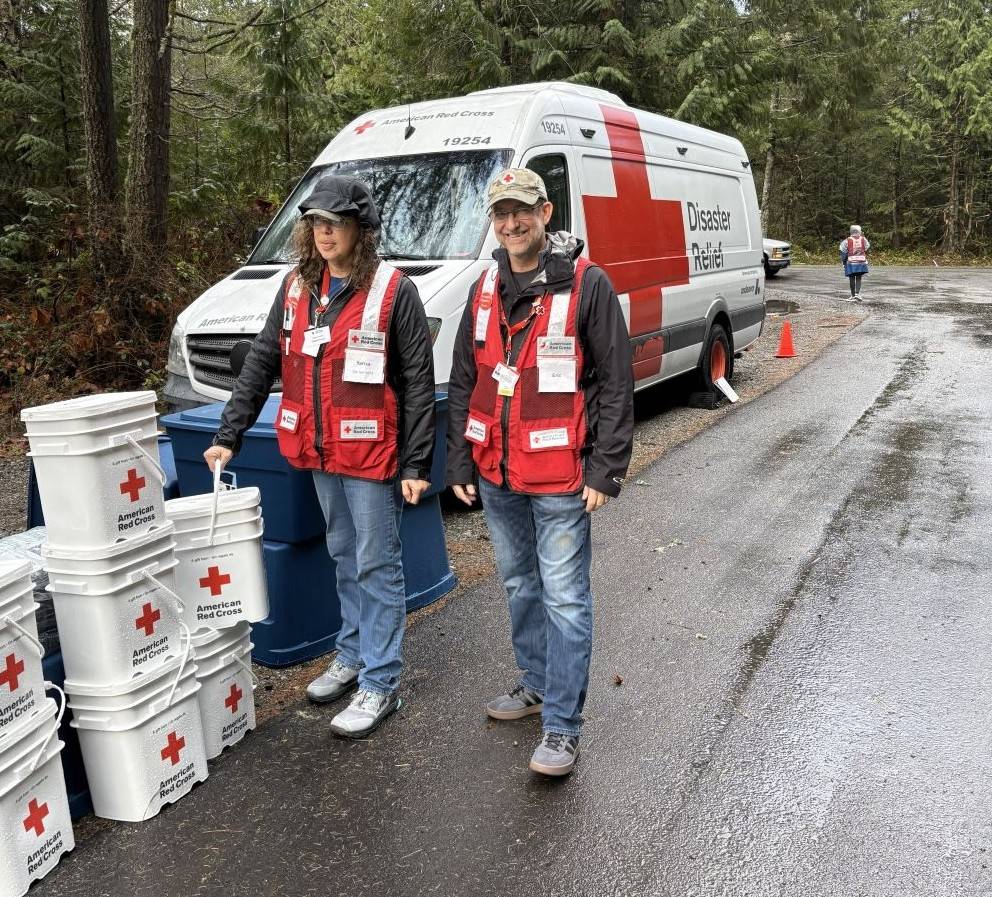 Two red cross volunteers walking in rain in front of a disaster response vehicle