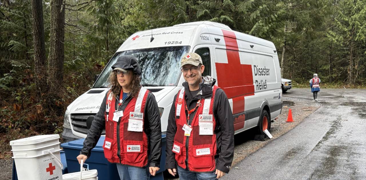 Two red cross volunteers walking in rain in front of a disaster response vehicle