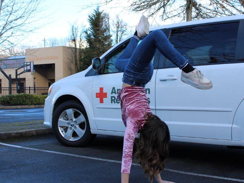 girl doing cartwheel in front of red cross vehicle