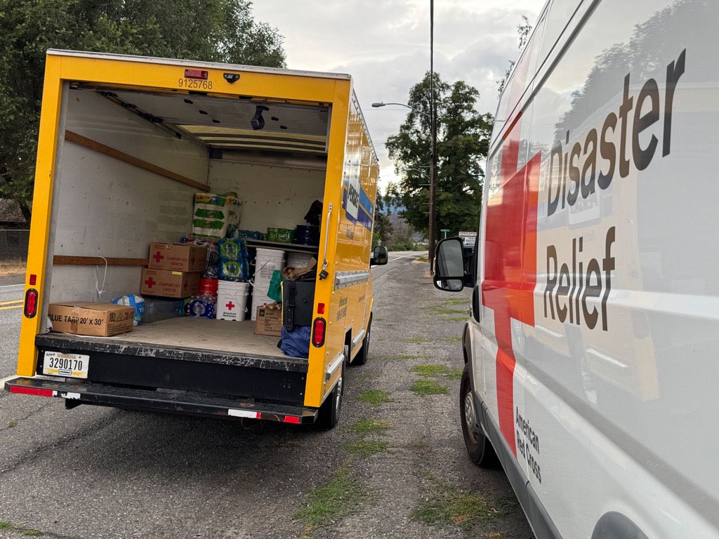 Red Cross Disaster Relief van parked next to a moving truck with it's back door open and disaster relief items in the back.