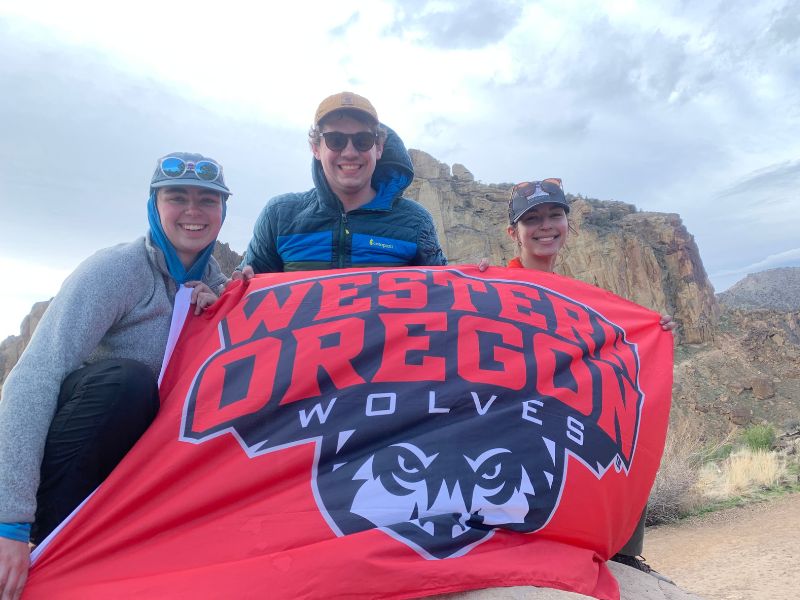 students happily holding western oregon university flag in mountains