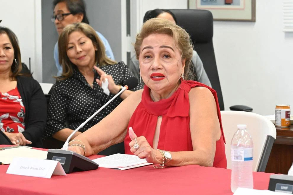 Chita Blaise, sitting at a table with a mic, speaks during a press conference.