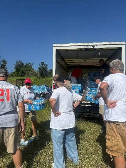 a group of volunteers unloading water bottles from the back of a moving truck.