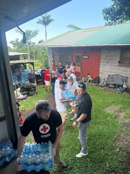 a group of volunteers, in an assembly line, unloading water bottles from the back of a moving truck.