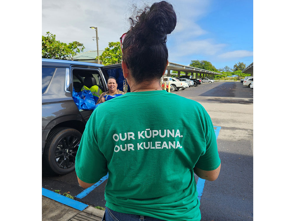 the back of a Red Cross volunteer with shirt that says, "Our Kūpuna. Our Kuleana."