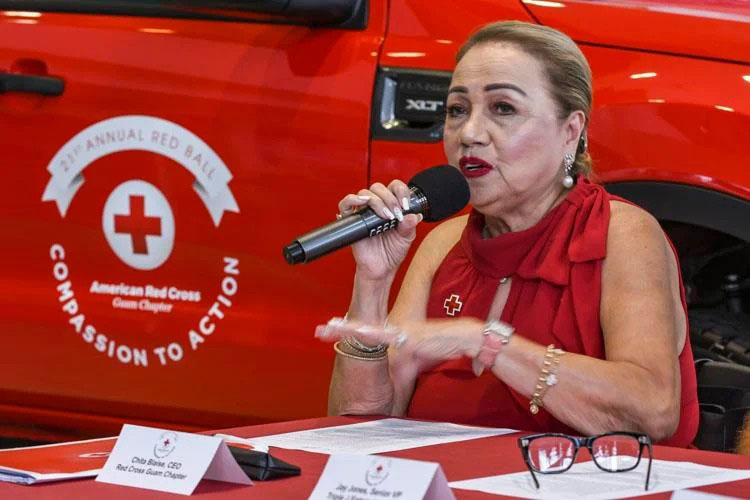 Chita Blaise sitting at a table, holding a mic and speaking into it.
