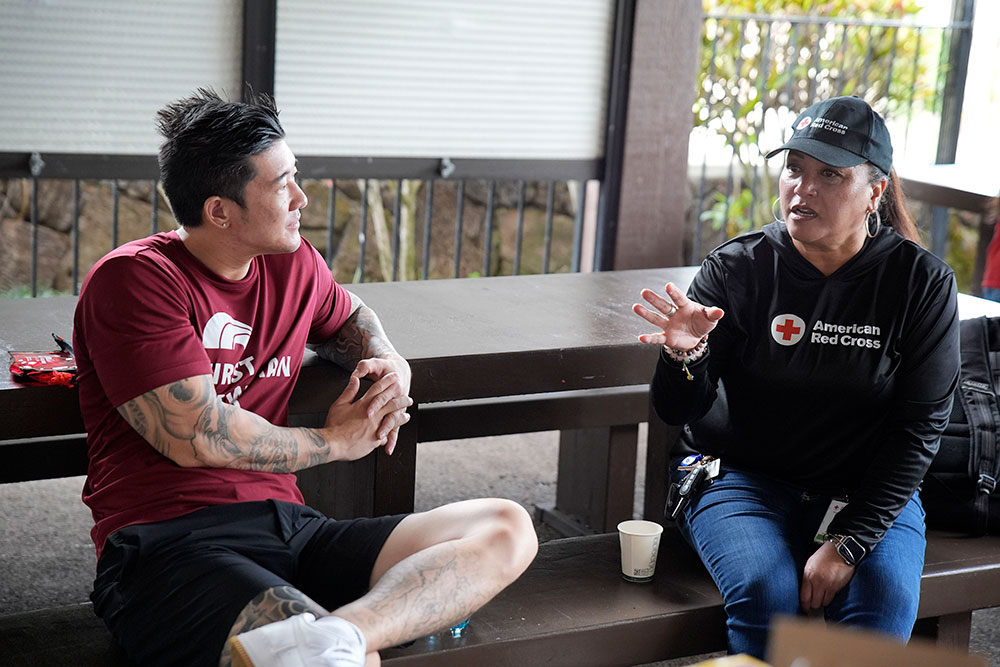 Red Cross volunteers speaking to each other while sitting on a bench.