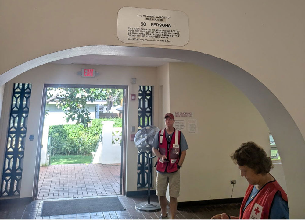 Two Red Cross volunteers standing in the Paki Hale shelter next to an open front door.
