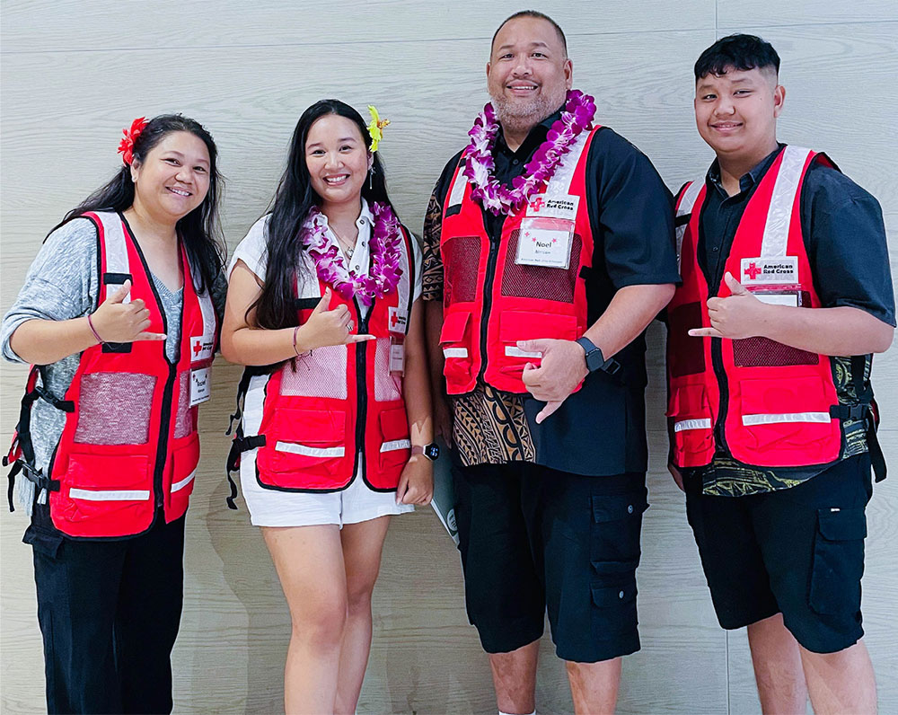 Four Red Cross volunteers wearing safety vests and giving the hang loose hand gesture.