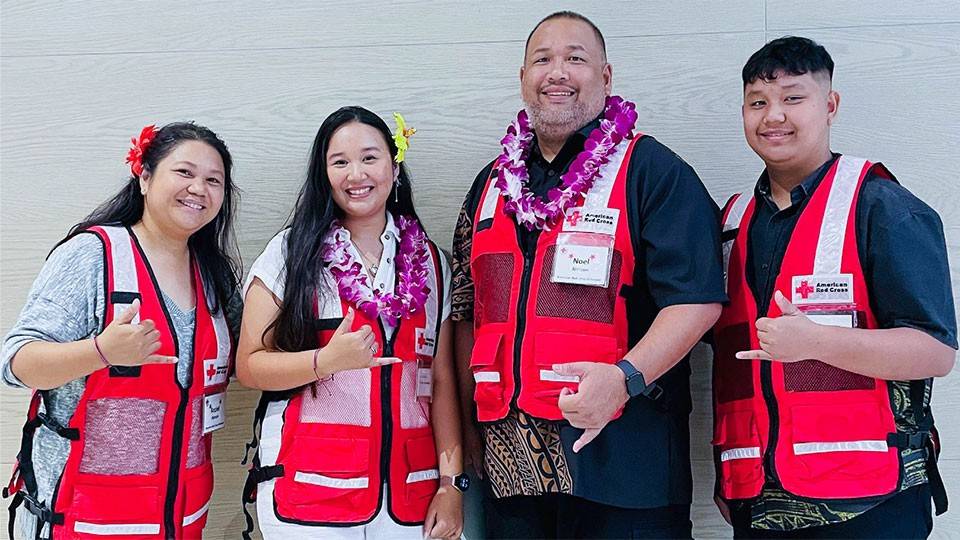 Four Red Cross volunteers wearing safety vests and giving the hang loose hand gesture.