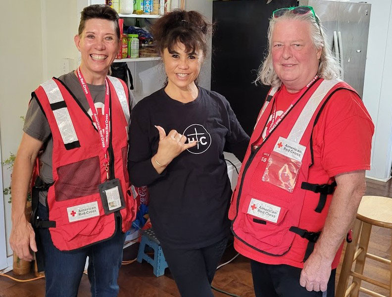 Red Cross volunteer Whitney McCarthy and another volunteer stand next to a resident who is giving a hang loose sign.