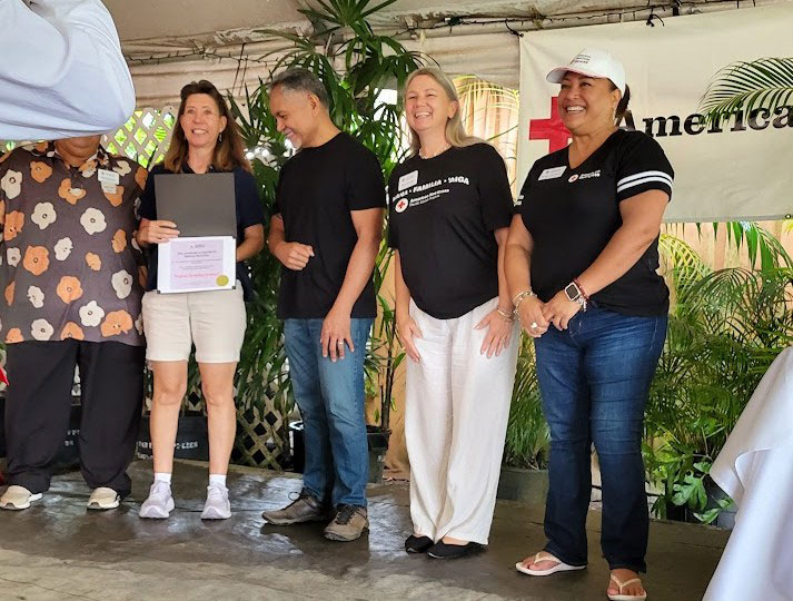 Whitney McCarthy holding and displaying the Spirit of the Pacific Award while standing next to red cross staff at an event.