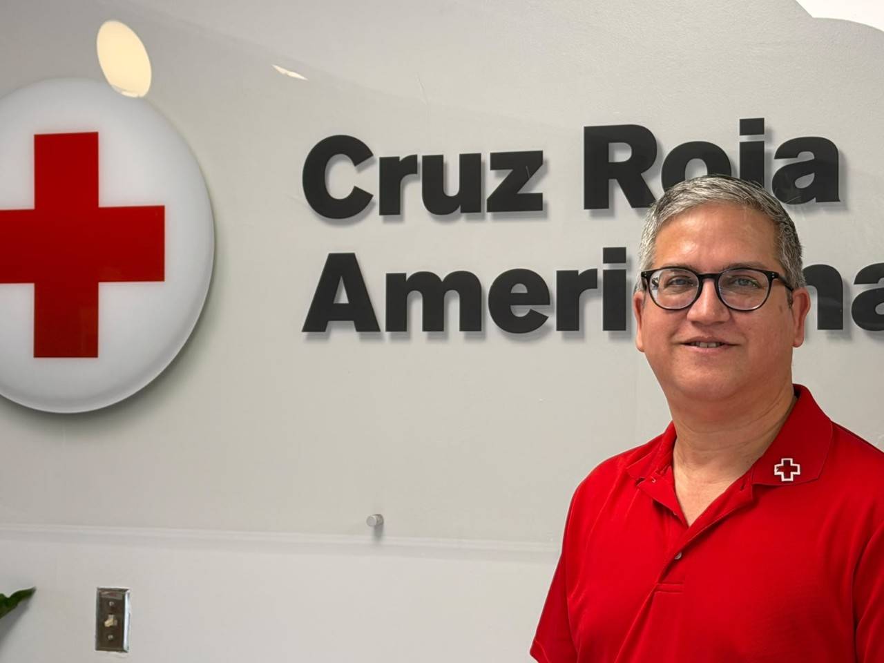 Daniel posa frente a un letrero de Cruz Roja Americana ubicada en la pared.