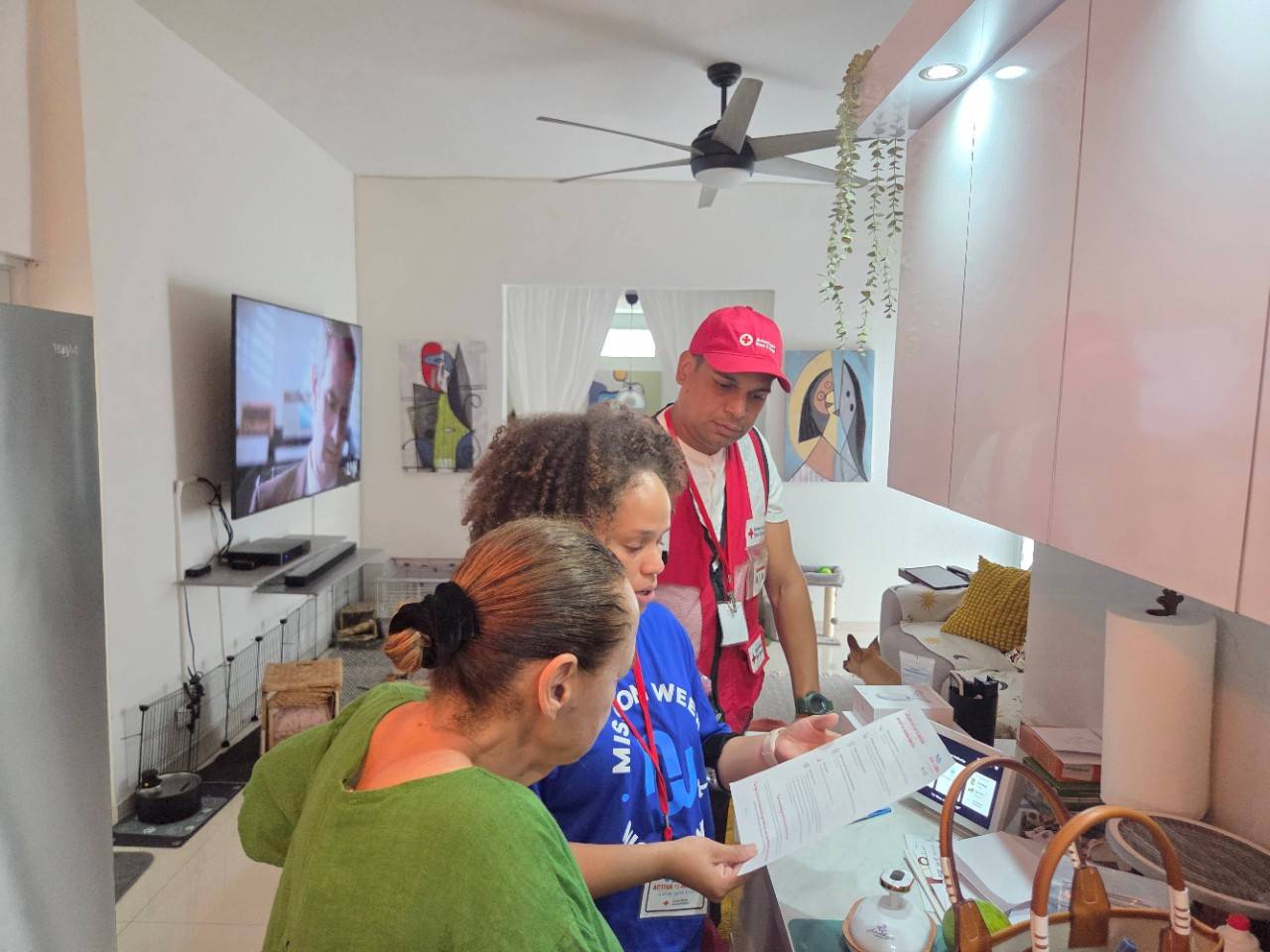 Empleada de Amgen Manufacturing Limited, Evelyn Cora, junto al voluntario de la Cruz Roja, Ebidí Vázquez, repasan algunos consejos para prevenir incendios dentro del hogar con una de las residentes impactadas con la campaña de instalaciones de detectores de humo. 