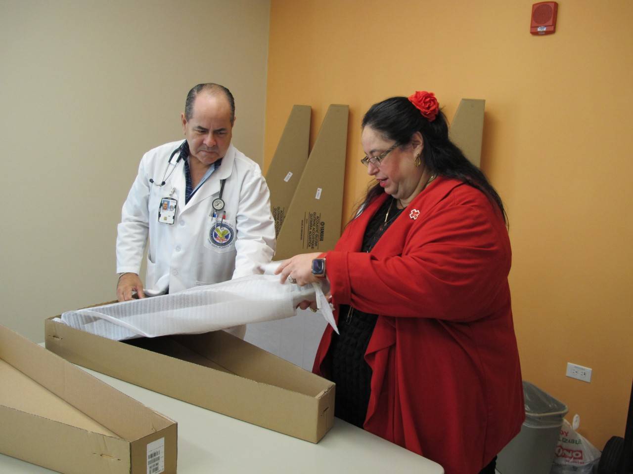 Foto del director médico de la Clínica de Ponce abre una de las cinco guitarras donadas con la directora de Servicio a las Fuerzas Armadas de la Cruz Roja Americana.