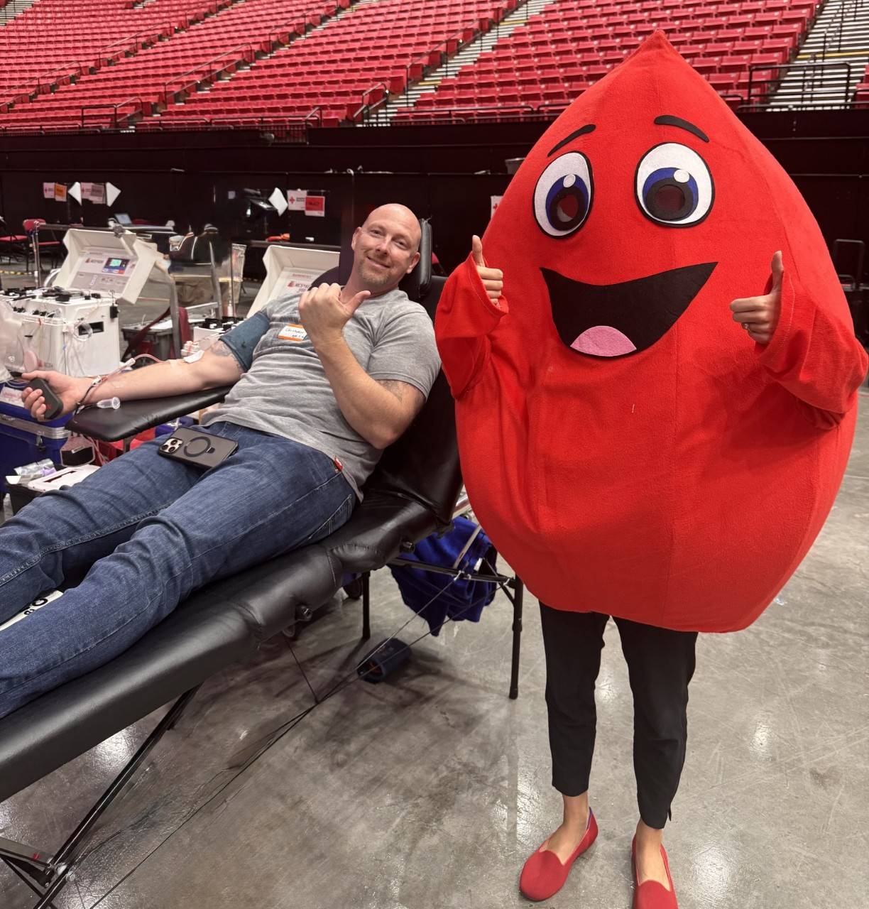 Blood donor Christopher donating and posing with the Buddy the Blood Drop mascot