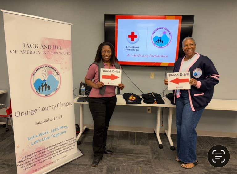 Two individuals smile and hold blood drive signs.