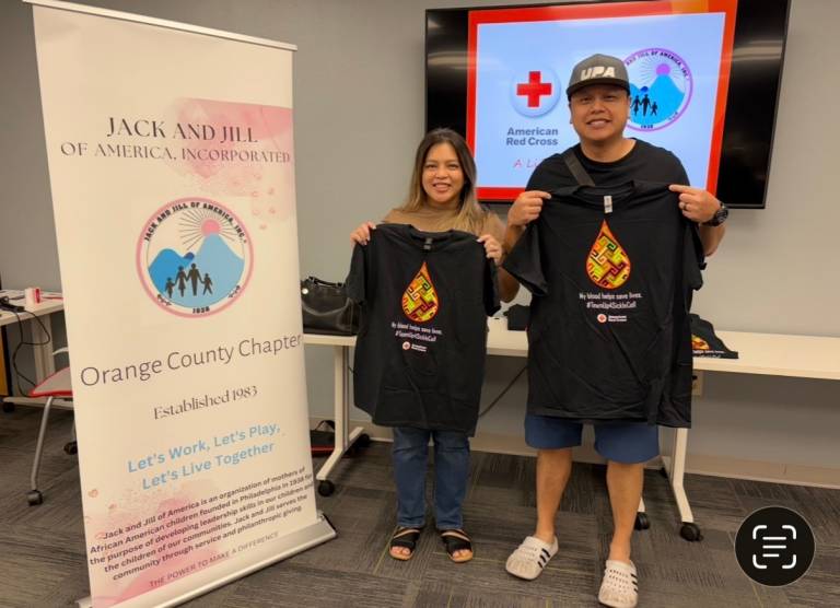 Two blood donors smile and hold up t-shirts.