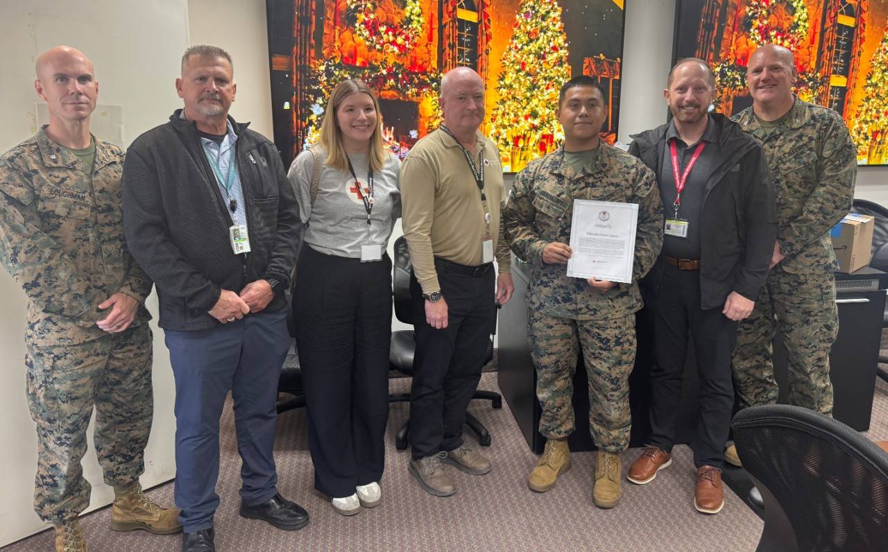 A Marine holding a certificate of merit stands for a photo with other Marines and civilians