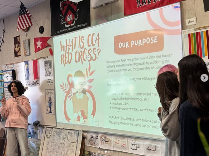 A classroom presentation on the CCA Red Cross. The speaker, Helen Afshar, smiles while presenting slides titled "What is CCA Red Cross?" to engaged students.