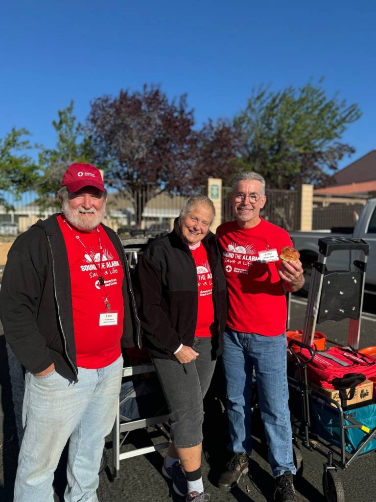 Three Red Cross volunteers smiling with equipment next to them.