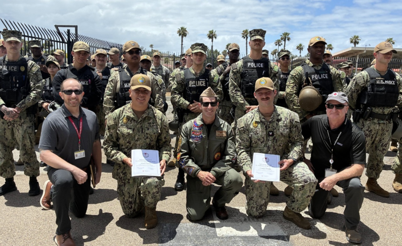 Service members pose with Red Cross representatives after receiving American Red Cross Lifesaving Awards, with fellow military personnel gathered behind them outdoors.