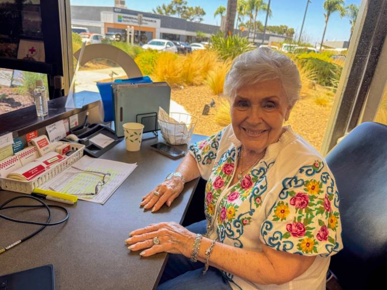 Woman smiling at a desk with a window behind her.