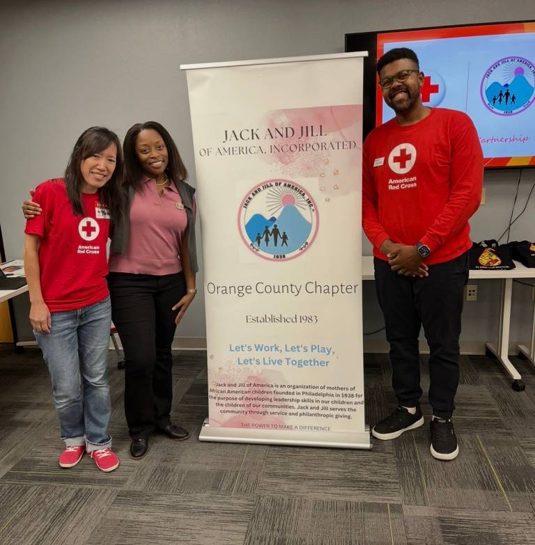 Three individuals in Red Cross t-shirts gather around a sign