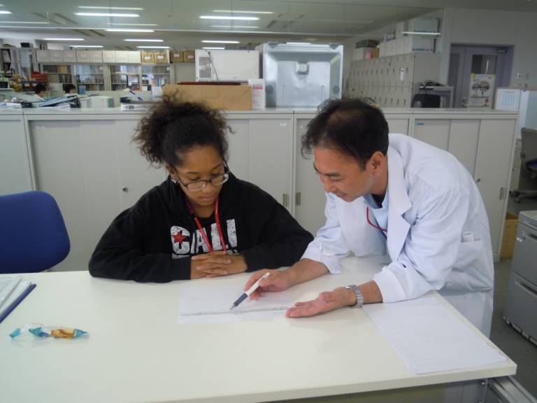 Myka is being shown something on a piece of paper by an individual in a white lab coat.