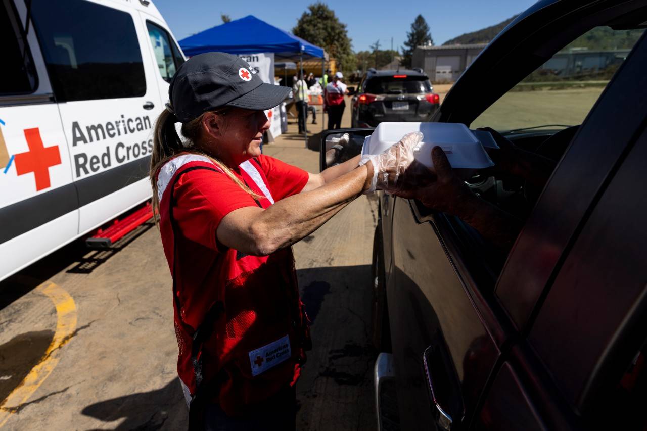 October 10, 2024. Swannanoa, North Carolina.
American Red Cross volunteer, Susan Harrington, provides hot meals to a family at a comfort care and distribution site in Swannanoa, North Carolina. The Red Cross was on site to provide hot meals and supplies like comfort kits containing hygiene items, ready-to-eat meals, blankets and water to help people recover from the devasting impact of Hurricane Helene across Western North Carolina. Since Hurricane Helene wreaked havoc on Western North Carolina, the Red Cross is working tirelessly to provide shelter, food, water, relief supplies and comfort to those coping with the unimaginable destruction left behind by Hurricane Helene. Hundreds of Red Crossers and our partners have provided meals, snacks and relief items like cleaning and hygiene items for thousands of families affected by Helene.
Photo by Scott Dalton/American Red Cross

