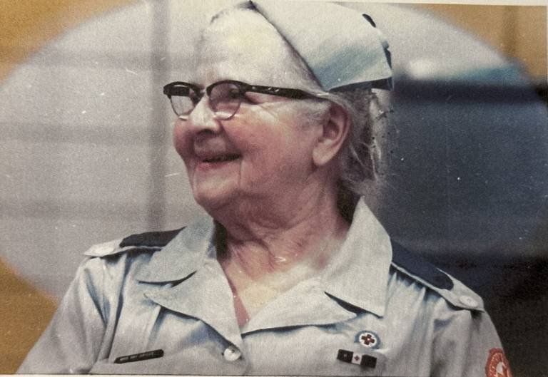 Woman wearing glasses and Red Cross uniform smiles while looking to the side