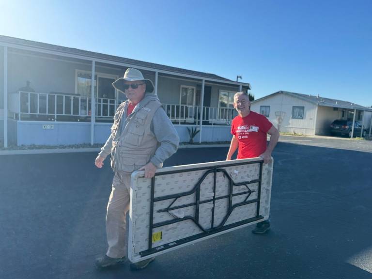 Two volunteers carrying a table in a neighborhood.