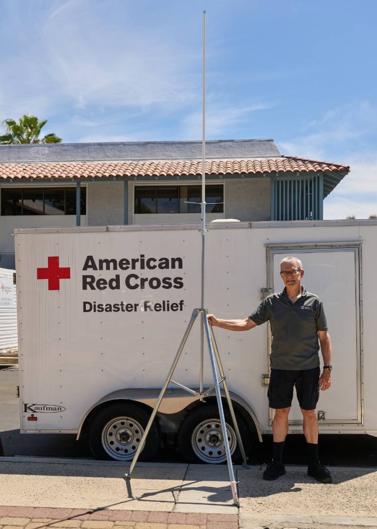 Red Cross volunteer stands next to antenna infront of Disaster Relief trailer.