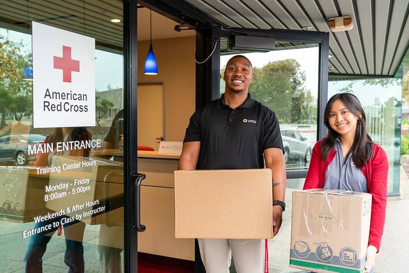 A man and woman stand in front of a door with a Red Cross logo on it