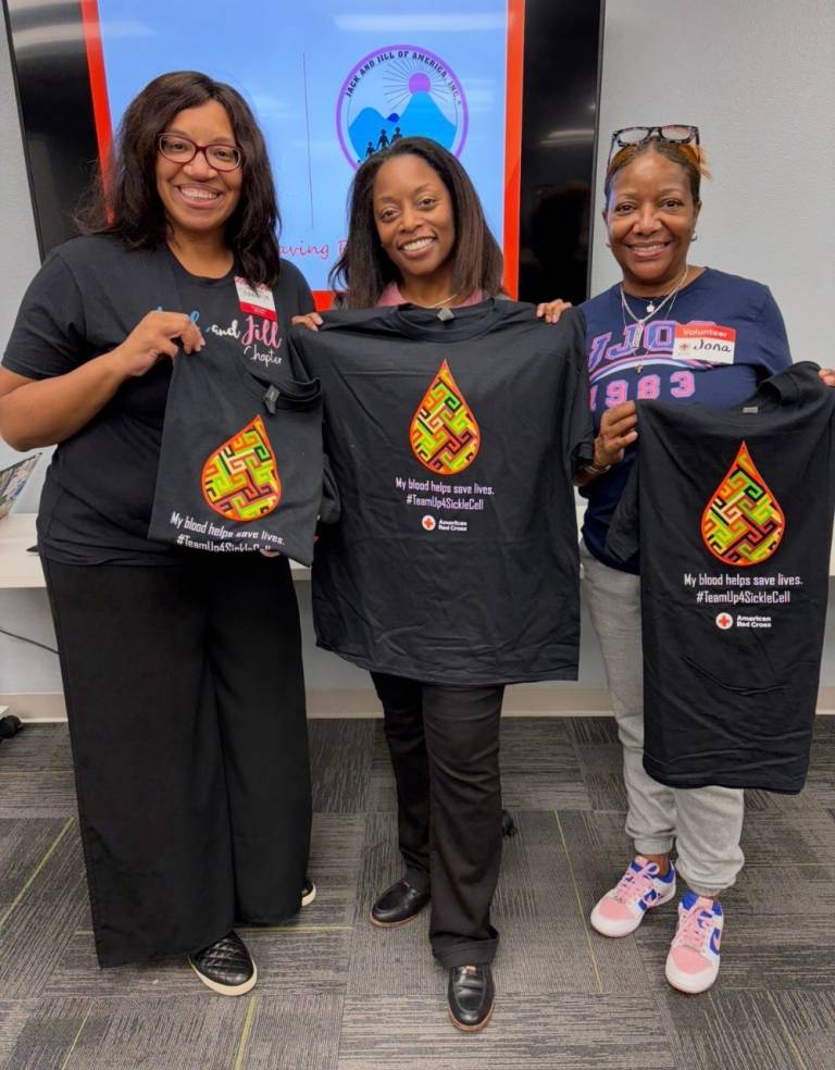 Three individuals hold up t-shirts and smile.