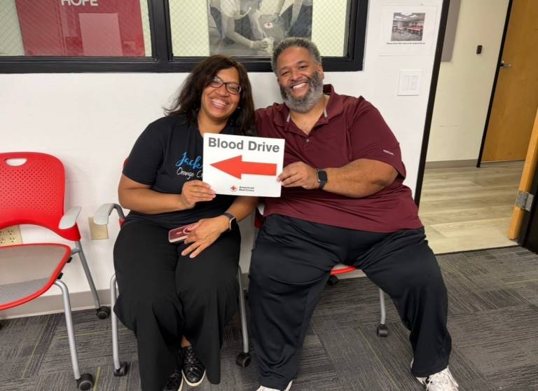 Two individuals smile and hold a blood drive sign.