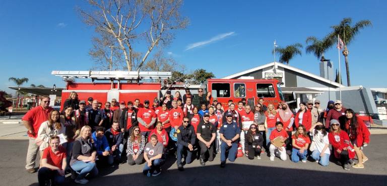 Group of Red Cross volunteers in front of a firetruck in a neighborhood.