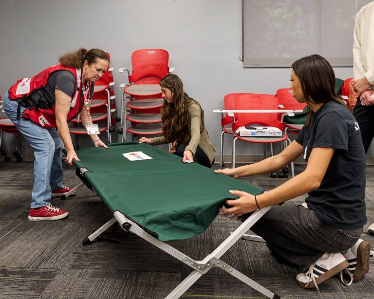 One adult and two youth volunteers set up a disaster cot.